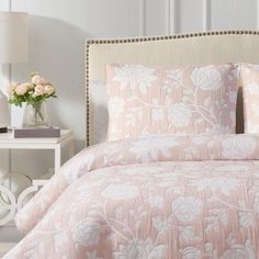 a bed with pink and white comforters in a bedroom next to a night stand