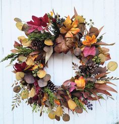 a wreath is hanging on the side of a white wall with autumn leaves and pine cones