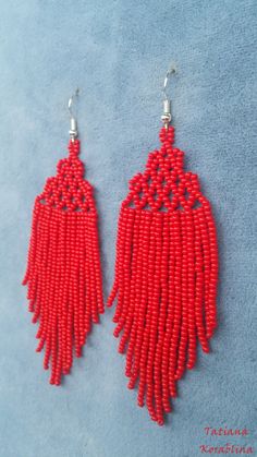 red beaded earrings with fringes hanging from hooks on a blue background, close up