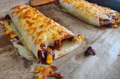 two burritos with cheese and other toppings sitting on a baking sheet next to a spatula