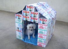 a small white dog sitting in a cardboard house made to look like it has cans on the roof