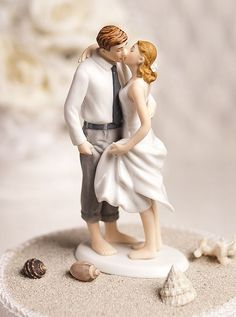 a bride and groom figurine kissing on top of a cake with seashells