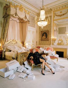 a woman sitting on a chair in a room with boxes around her and a chandelier hanging from the ceiling