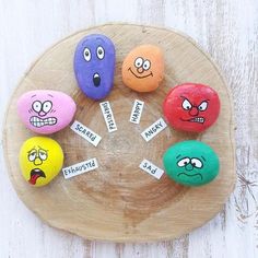 five rocks with faces painted on them sitting on a wooden plate