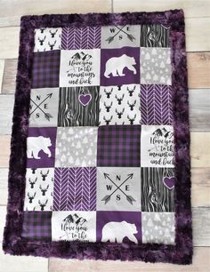 a purple and white patchwork quilt with bears, arrows, hearts, and words on it