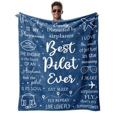 a man holding up a blue blanket with words on it that say best pilot ever