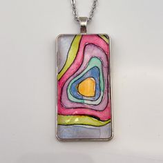 The lines in these paintings remind me of a topographical map. I imagine each of these pendants as a representation of a unique island that would be perfect for escaping the daily stressors of life. Six unique pendants were painted with these colors, and each is truly one of a kind! This pendant measures 1" wide by 2" tall (25mm x 50mm) and comes on an 22" chain. Jewelry comes on a presentation card in a white organza bag, ready to be gifted. Artistic Multicolor Abstract Jewelry, Artistic Multicolor Abstract Design Jewelry, Artistic Multicolor Jewelry With Abstract Design, Artsy Multicolor Round Pendant Necklace, Unique Multicolor Jewelry For Artistic Expression, Unique Multicolor Necklace, Artsy Abstract Design Jewelry As Gift, Multicolor Artistic Pendant Necklace, Unique Multicolor Rectangular Necklace