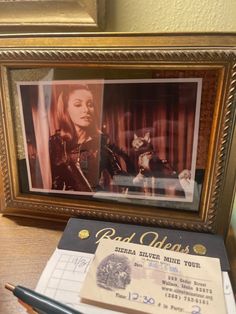 a framed photograph with a cat sitting on top of it next to a ticket and pen