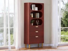 a tall red bookcase with three shelves in front of a white wall and windows