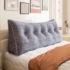 a large gray pillow sitting on top of a bed next to a white wall with pictures above it