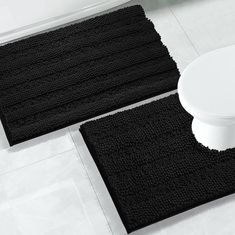 two black bath mats sitting on top of a bathroom floor next to a white toilet