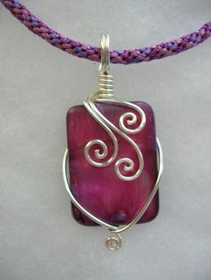 a purple and silver wire wrapped pendant with swirls on the front, sitting on a pink cord