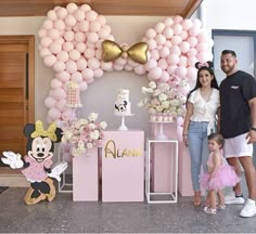 a man and woman standing next to a baby girl in front of a minnie mouse balloon arch