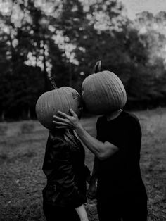 black and white photo of two people with pumpkins on their heads, one holding the other's head