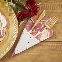 a place setting with red flowers and napkins on a wooden table, next to a gold fork and knife