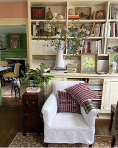 a white chair sitting in front of a book shelf filled with lots of books and plants