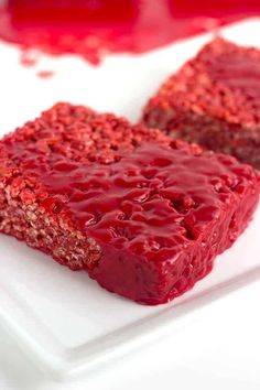 two pieces of red cake on a white plate with raspberry sauce in the background