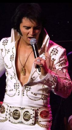 elvis presley singing into a microphone in his white outfit with gold and red decorations on it