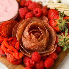 a wooden cutting board topped with lots of fruit and veggies next to a bowl of dip