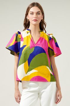 Introducing the whimsical wonder of the Rio Abstract Split Neck Poplin Top– where comfort meets color in a playful dance of poplin cotton perfection! Adorned with small ruffle ends on the shoulders and around the neckline plus a smooth outlined deep v-cut frame. So, go ahead, seize the day, and let your vibrant spirit shine through!- Ruffle detail- Split neckline- Short sleeves- Relaxed fit- Color: Khaki MultiSize + Fit - Model is 5'8" and wearing size XS- Measurements taken from size S - Chest: Playful Summer Blouse With Ruffles, Playful Ruffled Blouse For Summer, Colorful Cotton V-neck Tops, Vibrant Cotton Tops For Spring, Playful Ruffled Blouse For Spring, Vibrant Cotton Floral Print Top, Vibrant Floral Print Cotton Tops, Spring Multicolor Cotton Blouse, Multicolor Cotton Blouse For Spring