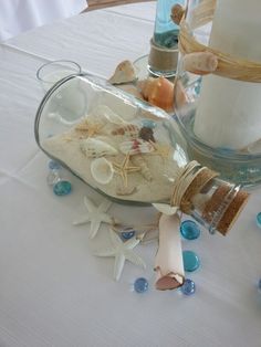 a bottle filled with sand and seashells sitting on top of a white table