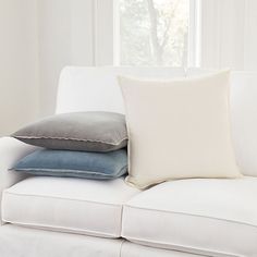 three pillows are stacked on the back of a white couch in front of a window