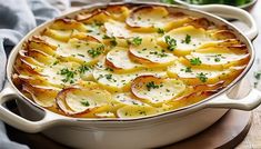 a casserole dish with potatoes and parsley in it on a wooden table