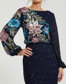 Adorned with intricate embellishments and a vibrant floral pattern, this gown exudes elegance and charm. The high neckline adds sophistication, while the multi-color design brings vibrancy and life to the ensemble. Mac Duggal Sequin fabric (100% polyester) Fully lined through body; semi-sheer unlined sleeves High neckline Long blouson sleeve Sequin floral pattern featured along bodice and sleeve Concealed back zipper Approx. 60" from top of shoulder to bottom hem Available in Black Multi, Nude M