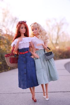 two dolls are standing next to each other on the sidewalk, one is holding a purse