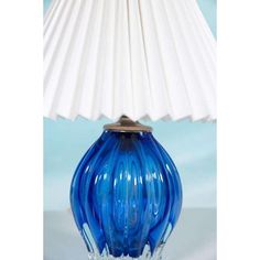 a blue glass lamp sitting on top of a table next to a white lampshade