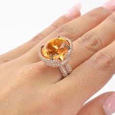 This exquisite ring features a stunning Citrine as the center stone, radiating vibrant hues of golden yellow. The Citrine is complemented by an array of White Zircon accent stones, adding a touch of brilliance and sparkle to the piece. The design showcases a luxurious rose gold-plated band, enhancing the warm tones of the Citrine. The intricate setting highlights the gemstone's natural beauty, making it a perfect statement piece for any occasion. This piece is inspired by the Art Deco era, known Orange Sapphire Round Ring, Luxury Gold Halo Ring With Gemstone, Fine Jewelry Yellow Topaz Ring With Halo Setting, Luxury Citrine Diamond Ring With Prong Setting, Yellow Topaz Halo Ring Fine Jewelry, Luxury Orange Rings With Prong Setting, Exquisite Gold Topaz Ring With Prong Setting, Luxury Yellow Gold Rings With Stones, Yellow Gold Topaz Ring With Gemstone Accents