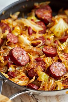 sausage and onions cooking in a skillet on a wooden table with utensils