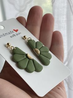 a pair of green leaf shaped earrings on a white card with a hand holding it