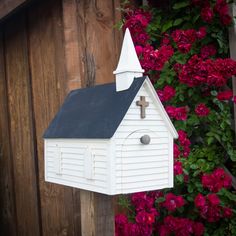 a small white church with a cross on it's steeple next to red flowers