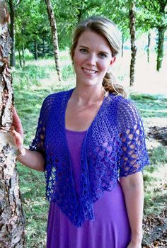 a woman standing next to a tree wearing a purple dress and crocheted shawl