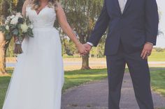 a bride and groom hold hands as they walk down a path