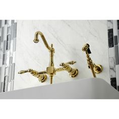 two golden faucets on the side of a white sink in a marble tiled bathroom