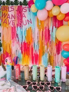 a table topped with lots of glasses next to a wall covered in balloons and streamers