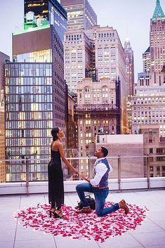 a man kneeling down next to a woman on top of a roof with rose petals