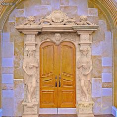 two wooden doors in front of a stone building with statues on it's sides