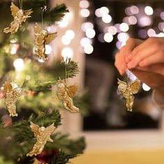 someone decorating a christmas tree with gold angel ornaments