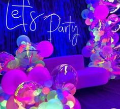 balloons and streamers are on display in front of a neon colored backdrop that says let's party