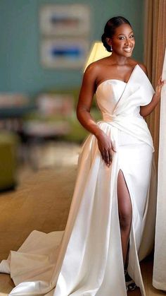 a woman in a white dress standing next to a curtain with her legs crossed and smiling