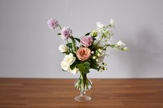 a glass vase filled with flowers on top of a wooden table next to a white wall