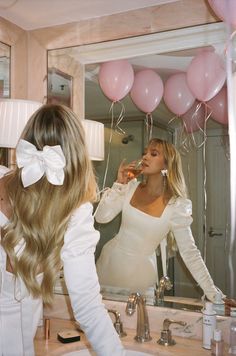 the woman is brushing her teeth in front of the mirror with pink balloons on it