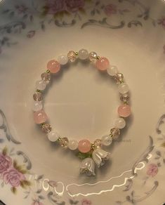 a pink and white bracelet with flowers on it sitting on top of a china plate