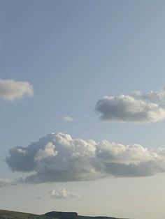 two people are flying kites in the sky on a grassy field with mountains and clouds