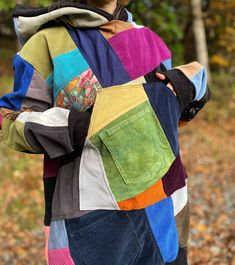 a person wearing a multi colored jacket in the woods with their hands on their hips