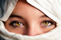 a woman with yellow eyes is wearing a white shawl and looking at the camera