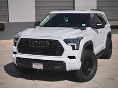 a white toyota truck parked in front of a building with garage doors and shutters